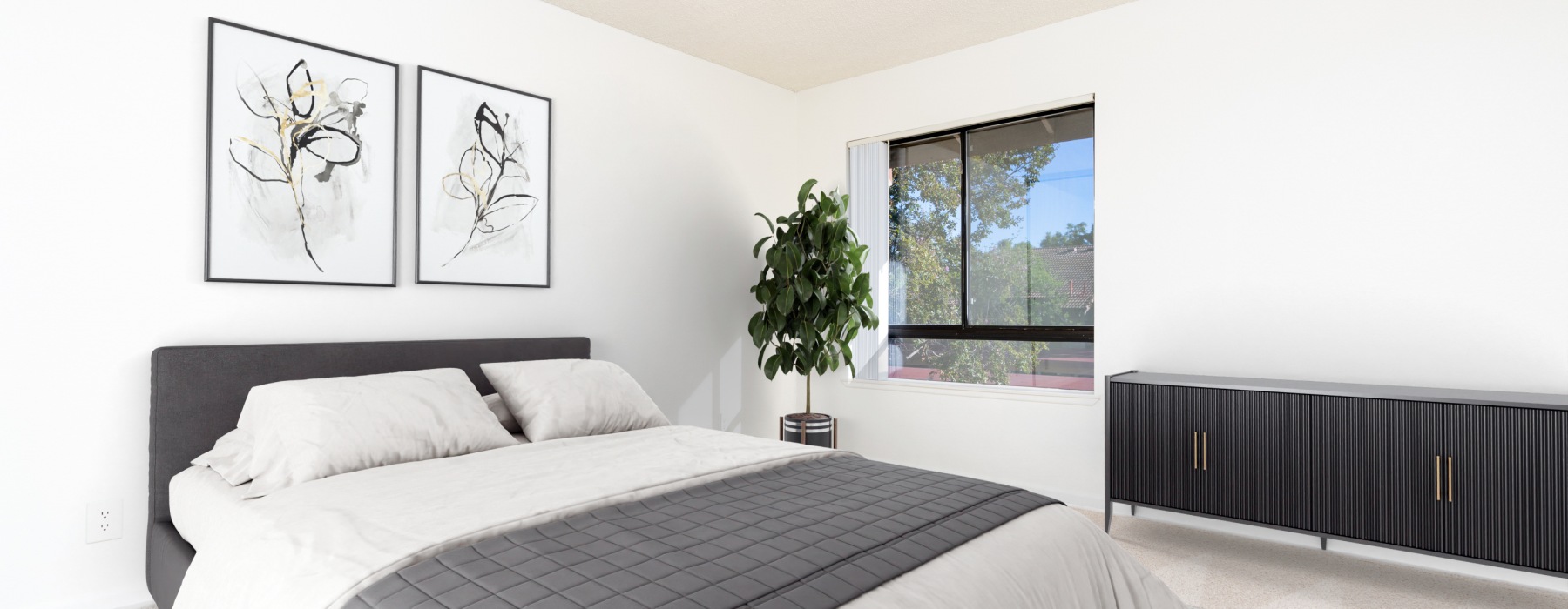 A bright, modern bedroom with a gray upholstered bed, white bedding, two abstract botanical art prints on the wall, a potted fiddle-leaf fig plant beside a large window, and a dark low-profile dresser to the right.