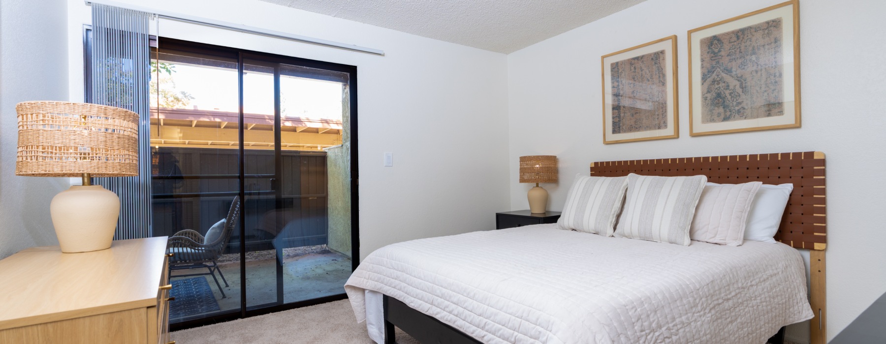 Bright bedroom with a woven leather headboard, white bedding, sliding glass patio door, and rattan lamps.