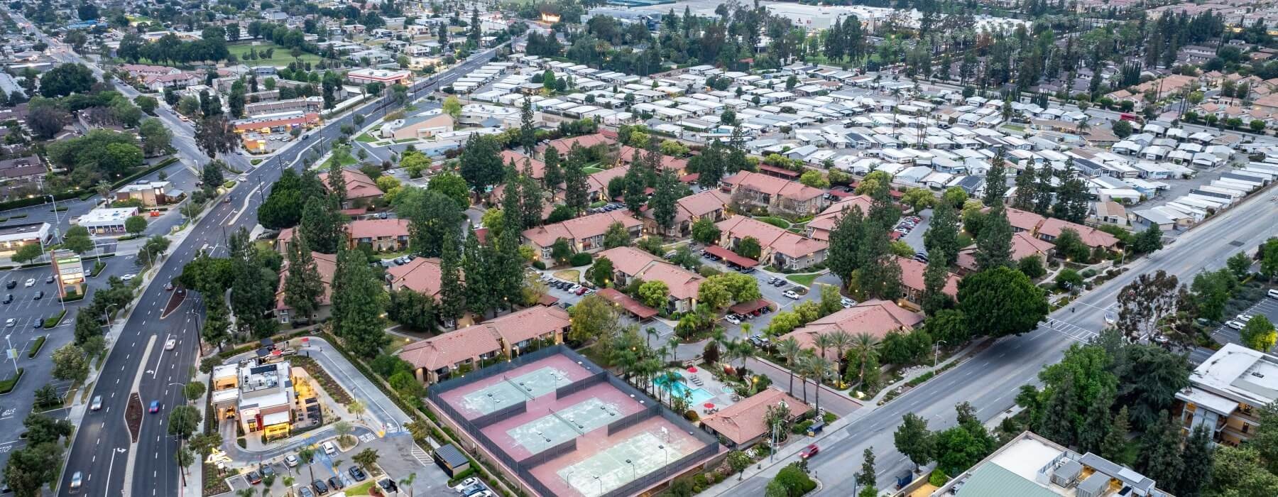 Aerial view of a red-tile-roofed residential complex with tennis courts and a pool, surrounded by suburban homes and tree-lined streets.
